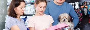 friendly cheerful glad family with little dog buying pet supplies in store