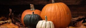 A closeup shot of pumpkins surrounded by brown leaves with a wooden background for Halloween
