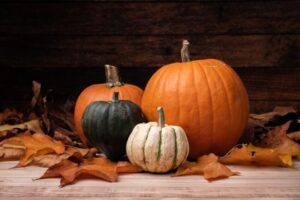 A closeup shot of pumpkins surrounded by brown leaves with a wooden background for Halloween